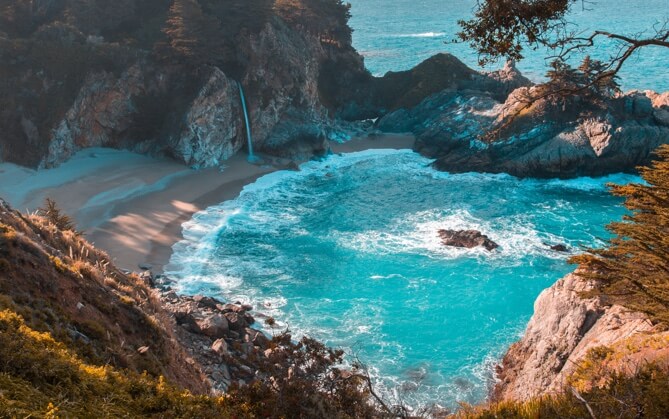 Image from a cliff of a cove with light blue water and a rocky shore